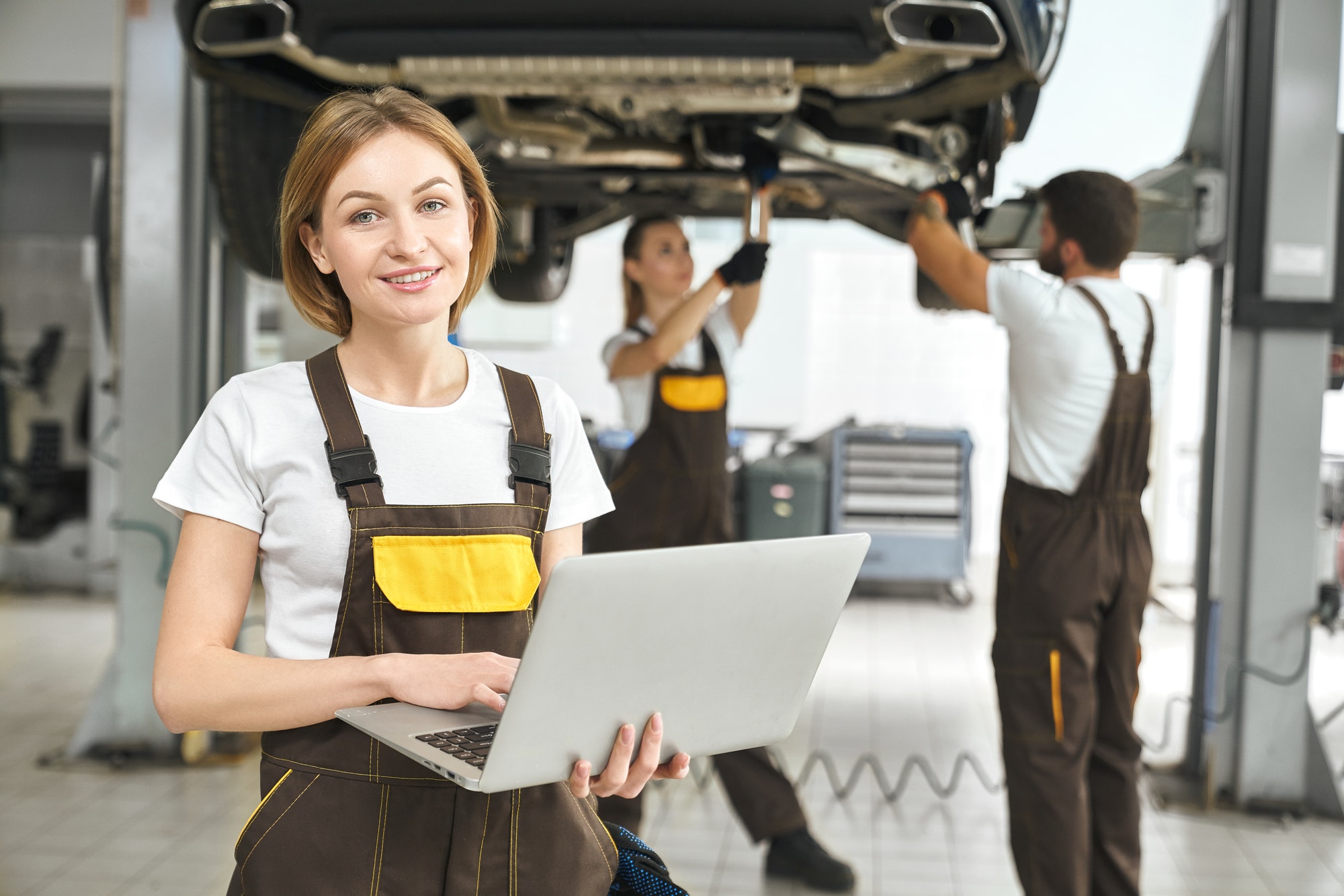 Pretty worker holding laptop, posing in autoservice