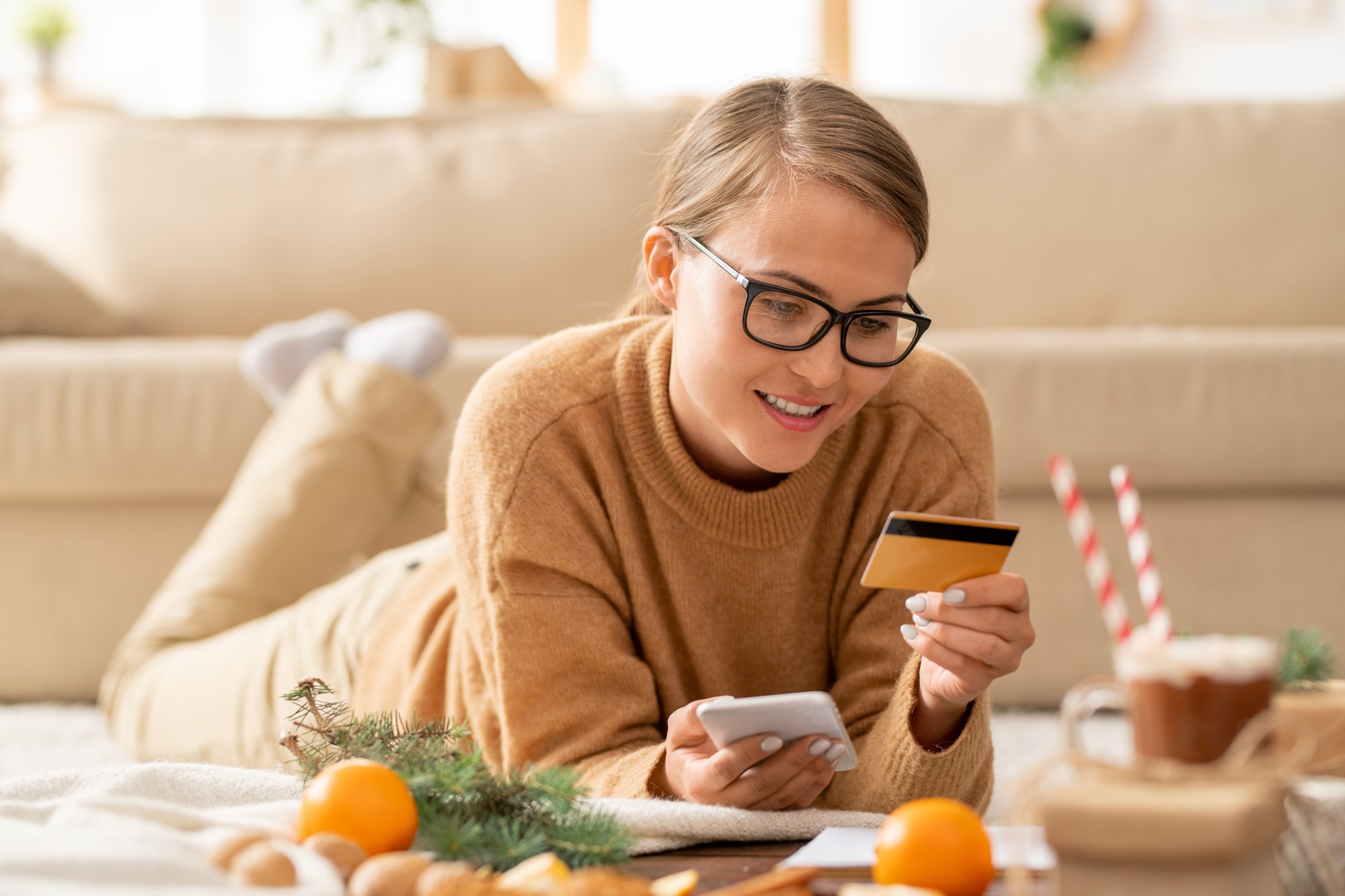 Young casual woman with smartphone and credit card looking at personal data