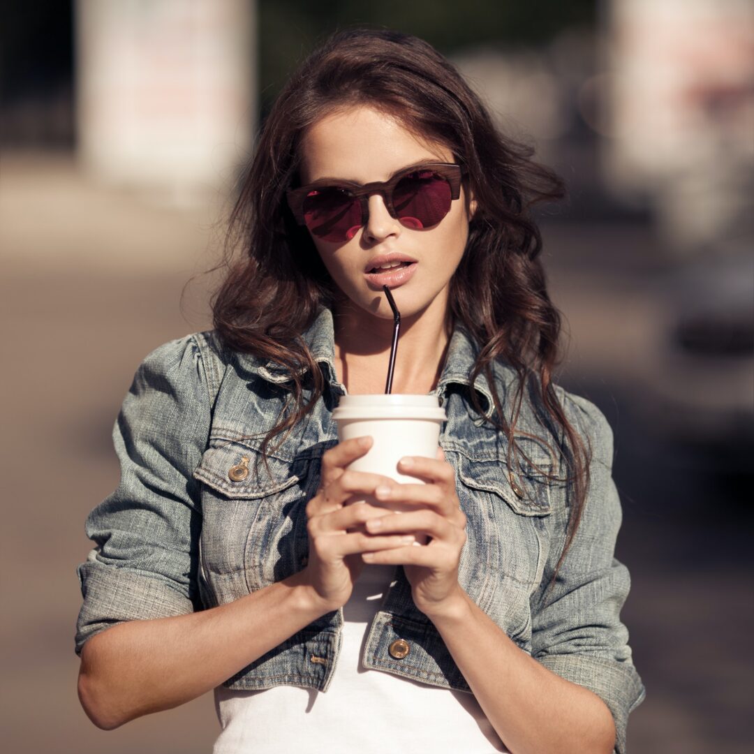 Young Woman Drinking Coffee From Paper Cup On A City Street
